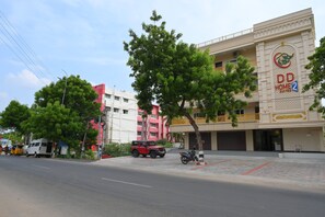 Un hotel con un letrero visible, una zona exterior techada y una calle con vehículos y peatones.