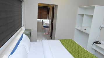A hotel room with a bed, a desk, a chair, a wardrobe, and a telephone.