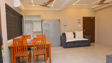 Una habitación de hotel con una mesa de comedor, sillas, un sofá, un ventilador de techo y una puerta.