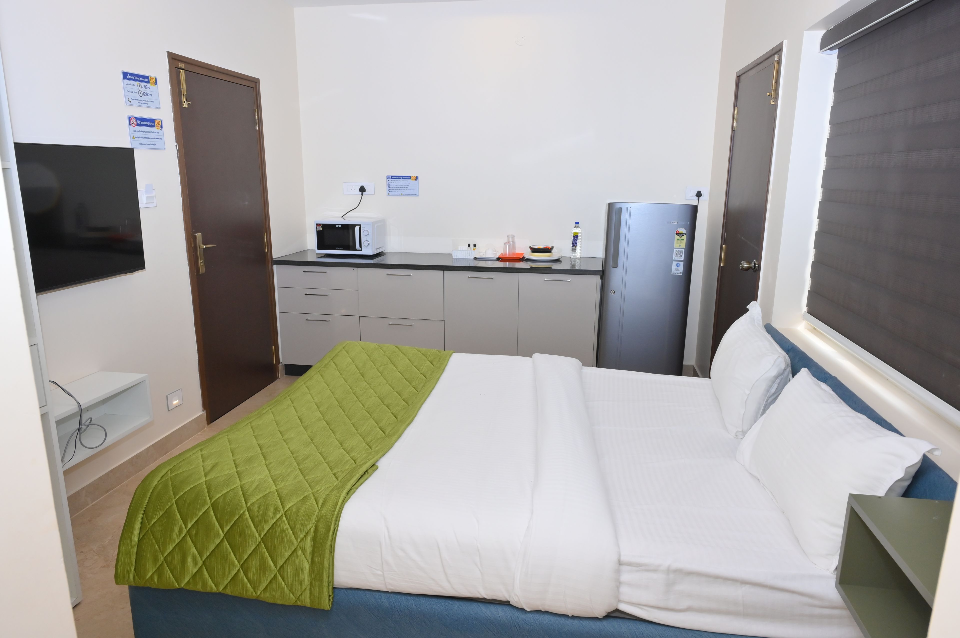 A compact hotel room with a bed, a kitchenette, a microwave, a refrigerator, and a television.