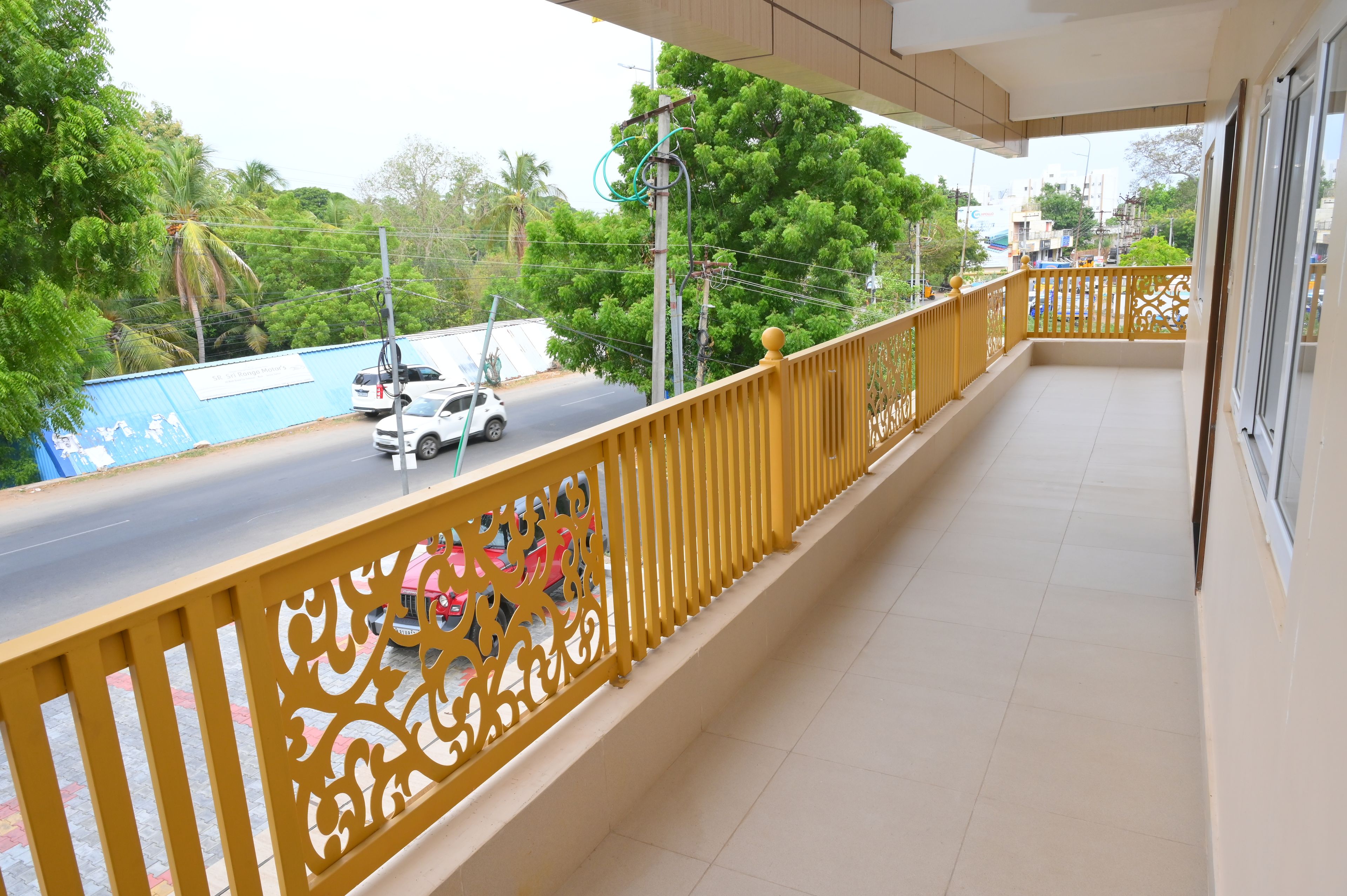 A balcony with a yellow railing, a view of a road with vehicles, and greenery in the background.