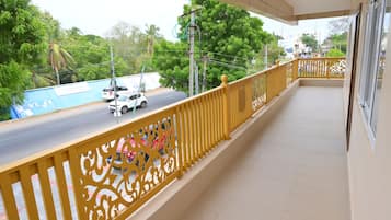 A balcony with a yellow railing, a view of a road with vehicles, and greenery in the background.