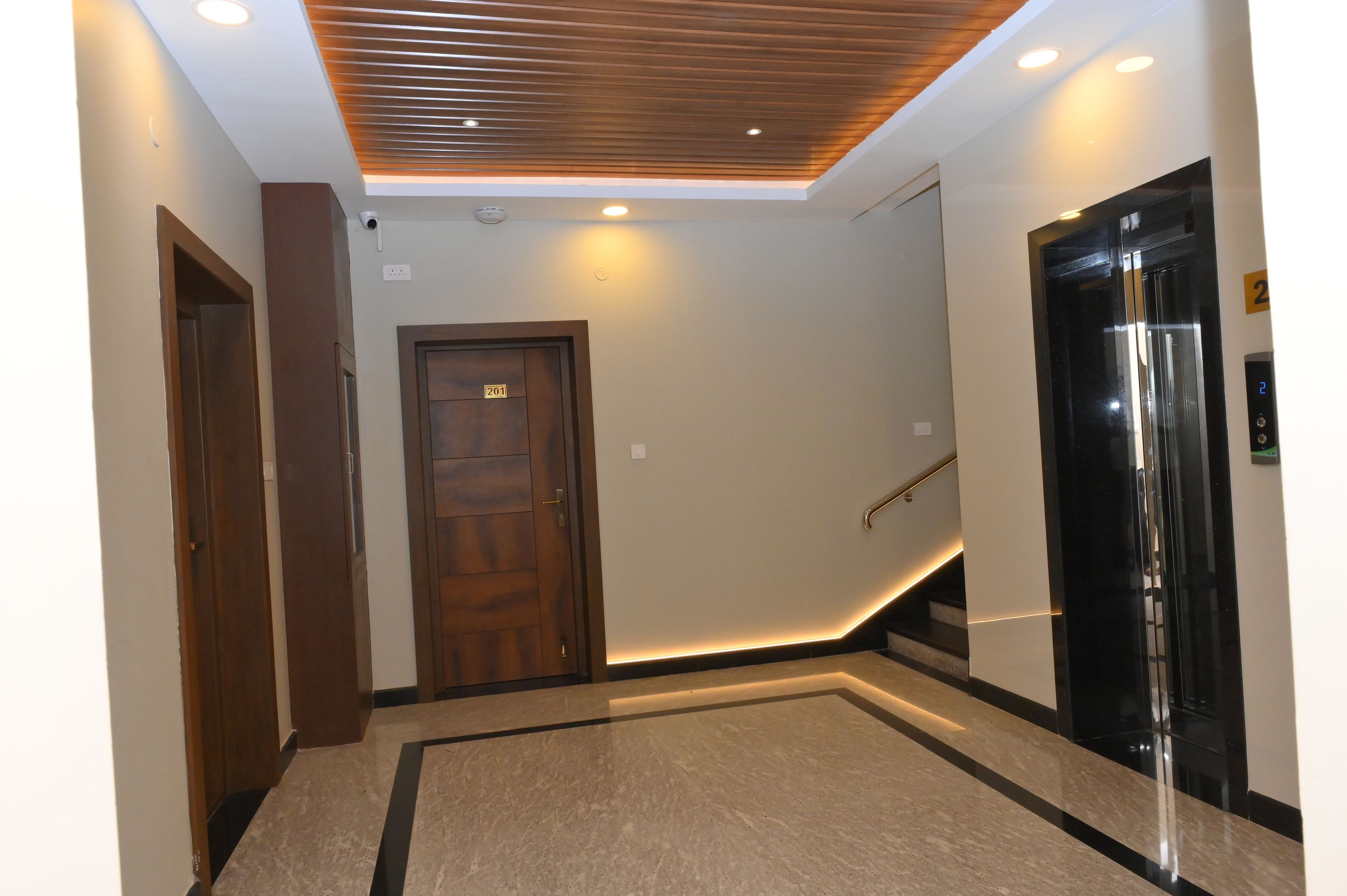 Un interior moderno con techo de madera, una puerta con la etiqueta '201' y un ascensor negro.