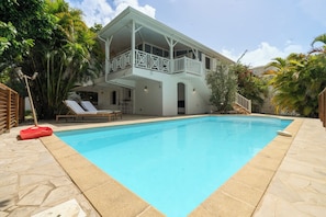 A two-story house with a swimming pool, a covered patio, and a garden with tropical plants. - Appartement Central View (Ducos)