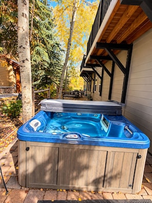 A hot tub in a wooden outdoor setting with a wooden deck and a building in the background. - Sun Bird Townhome - pet friendly (Ketchum)
