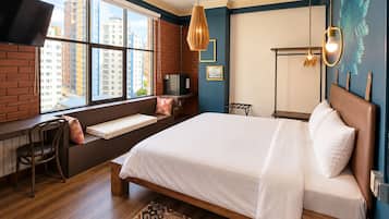 Ein Hotelzimmer mit einem großen Bett, einem Schreibtisch, einem Sessel, einem Fernseher und Blick auf Gebäude durch das Fenster.
