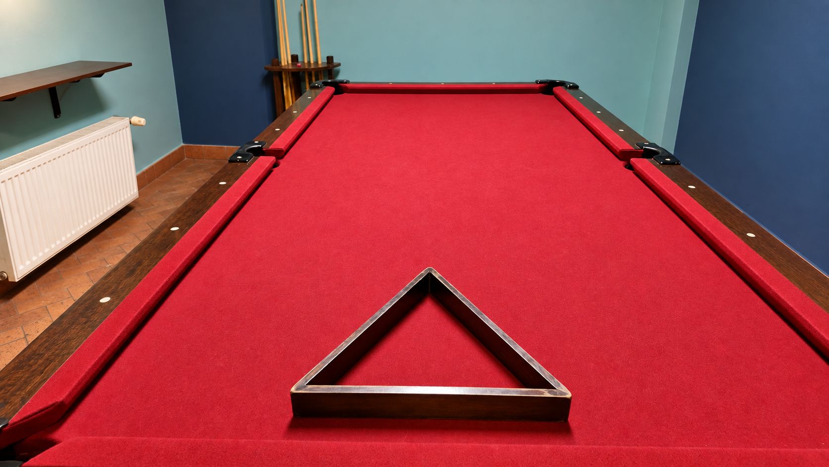 A pool table with a red felt surface and a triangular object in the center.