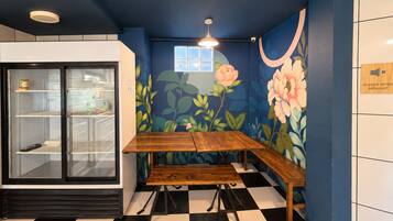 Una habitación con suelo a cuadros, un banco de madera, un refrigerador con puerta de vidrio y un mural floral en la pared.