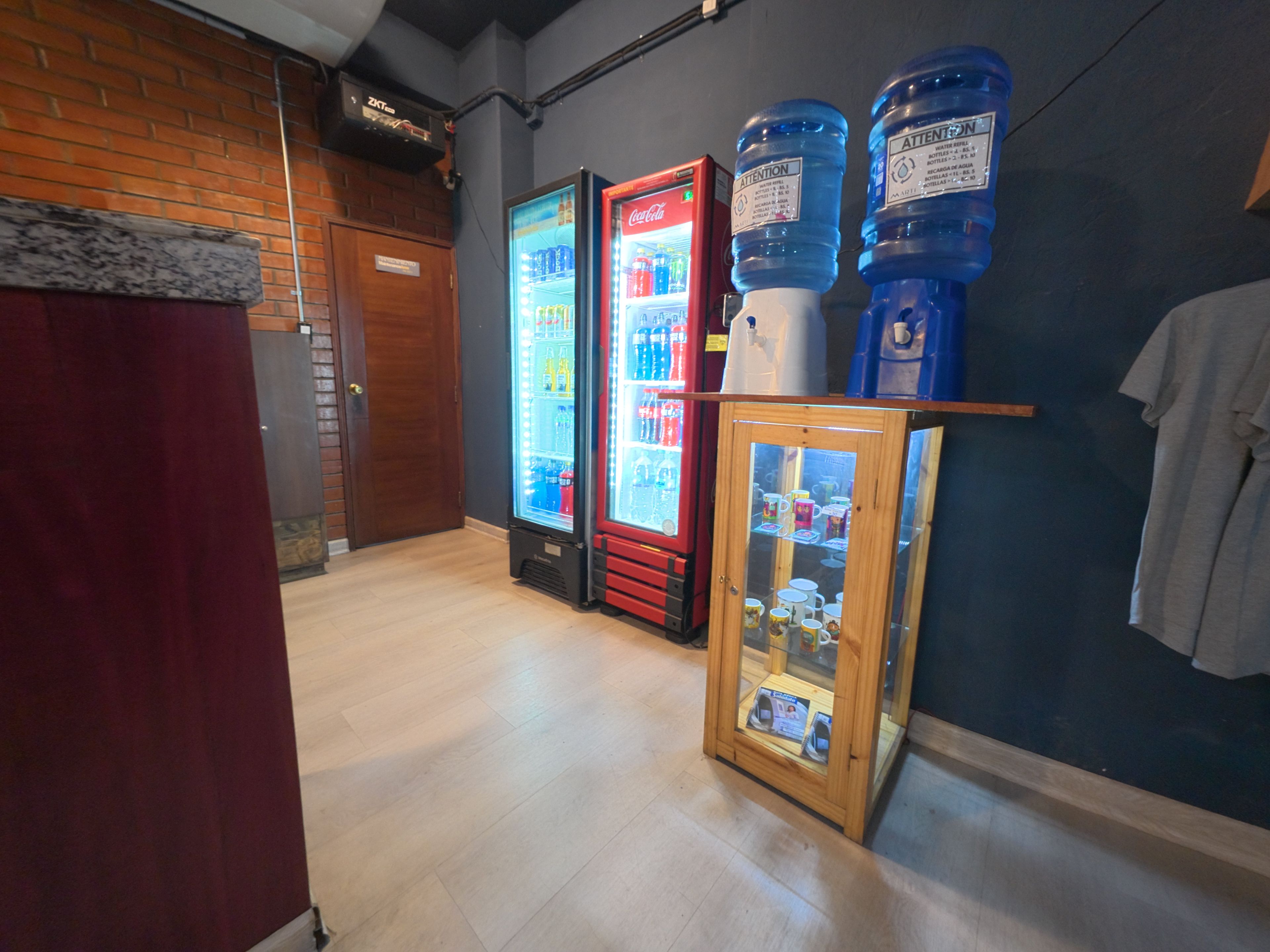 Ein Flur mit einem Getränkeautomaten, einem Kühlschrank und einer Vitrine mit Tassen.