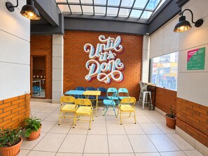Interior de una cafetería con un letrero que dice 'Until the Dawn', sillas amarillas y azules, y una pared de ladrillo.