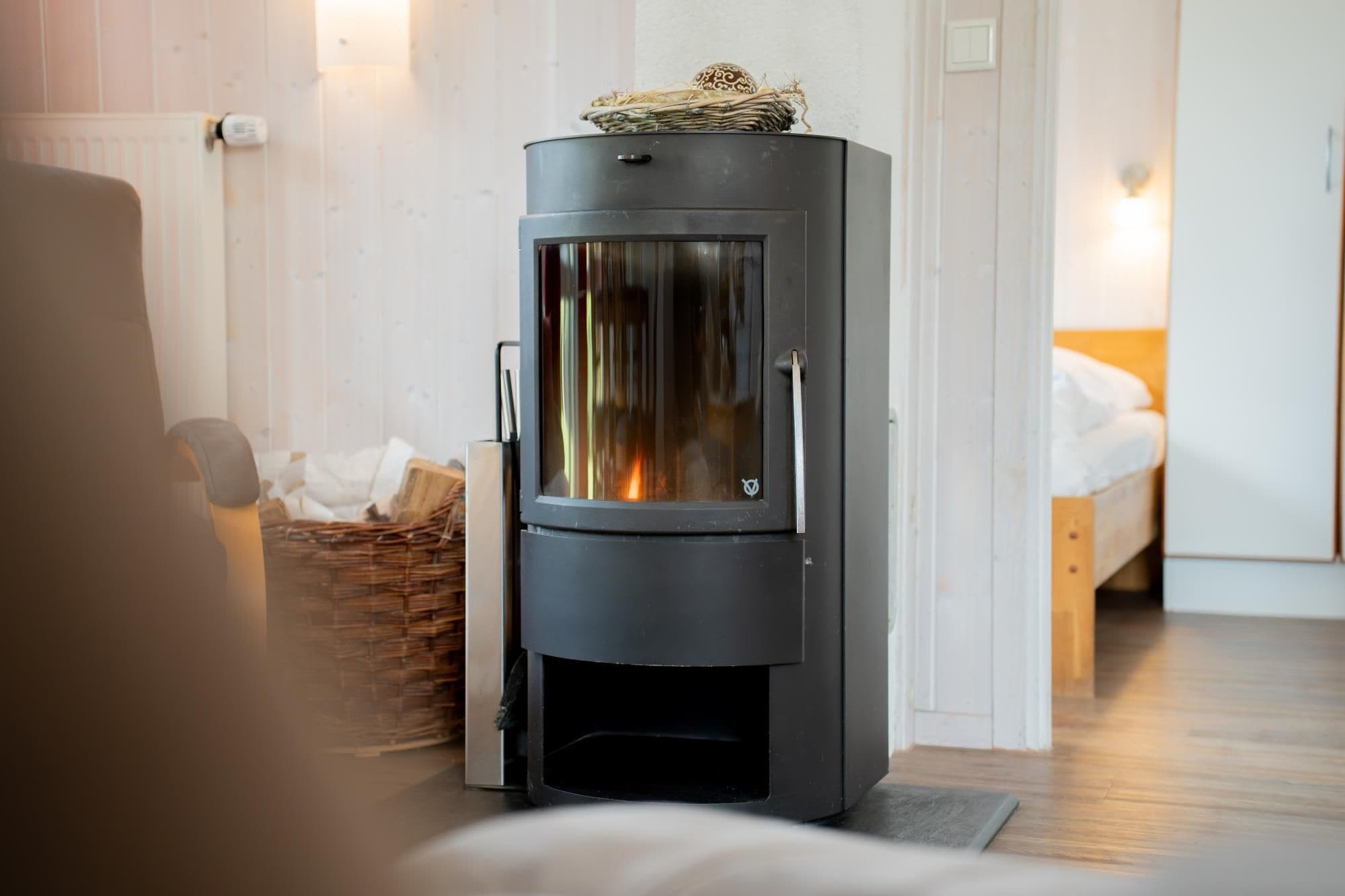 Un poêle à bois moderne dans une pièce comprenant un lit et un panier en osier.