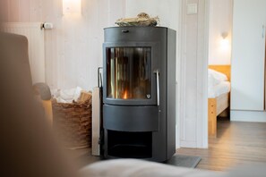 A modern wood-burning stove in a room with a bed and a wicker basket. - Vacation home for 6 people with a sauna and hot tub – fireplace, patio, and large garden (Otterndorf)