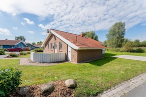 A single-story brick house with a red-tiled roof, a small front porch, and a well-maintained lawn. - Vacation home for 6 people with a sauna and hot tub – fireplace, patio, and large garden (Otterndorf)