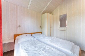 A single bed with white bedding in a room with wooden walls and a wooden ceiling. - Vacation home for 6 people with a sauna and hot tub – fireplace, patio, and large garden (Otterndorf)