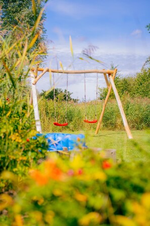 A swing set in a garden with a clear sky. - Vacation home for 6 people with a sauna and hot tub – fireplace, patio, and large garden (Otterndorf)