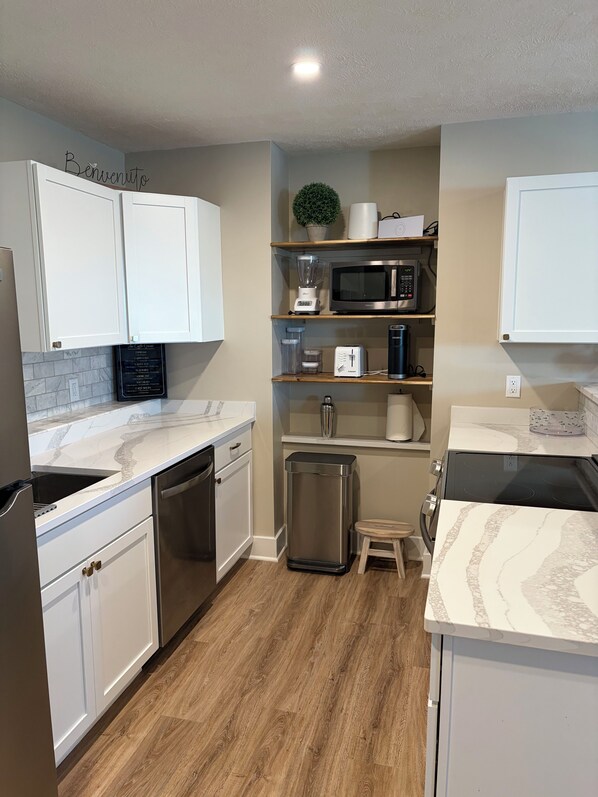 A modern kitchen with white cabinetry, a built-in microwave, a coffee maker, and a trash can.