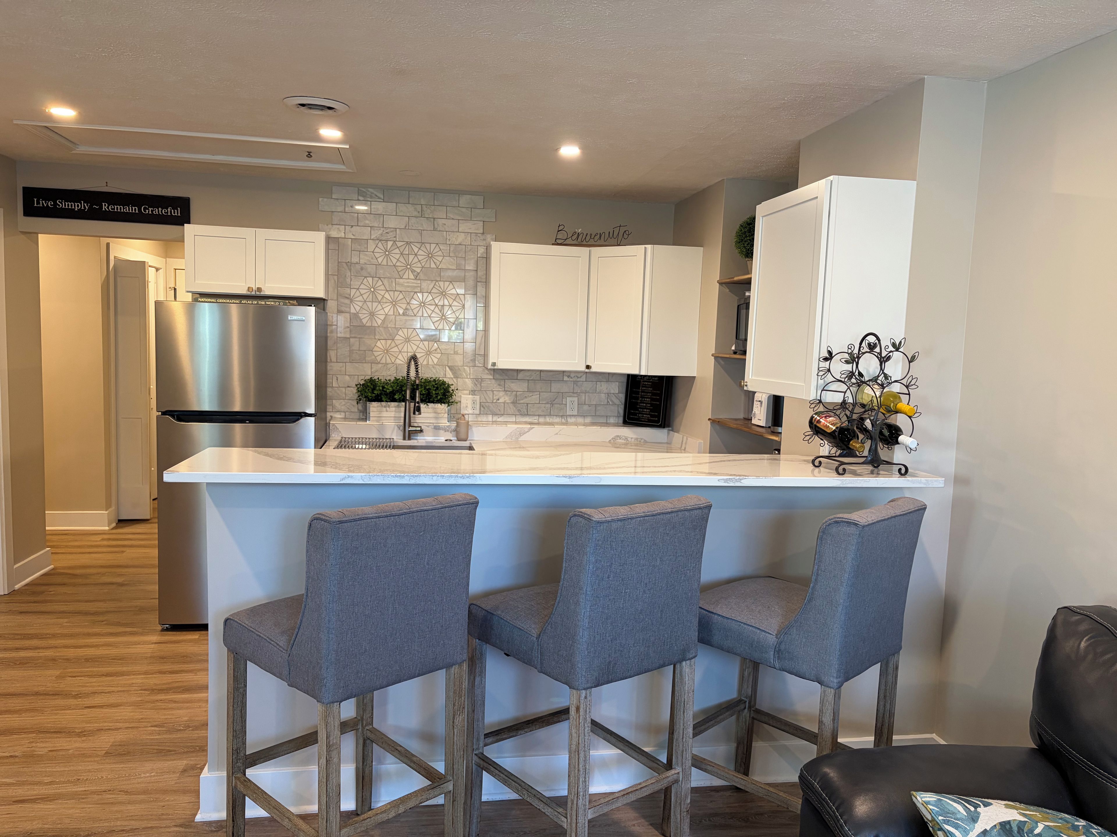 A modern kitchen with a central island, bar stools, stainless steel appliances, and a decorative backsplash.