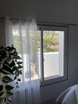 Et værelse med en skydedør til et udendørs område, en potteplante og en hvid gardin.