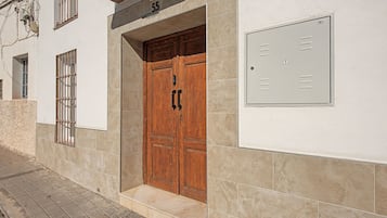 Een gebouwde ingang met een houten dubbele deur, een brievenbus en een technische kast aan de muur.