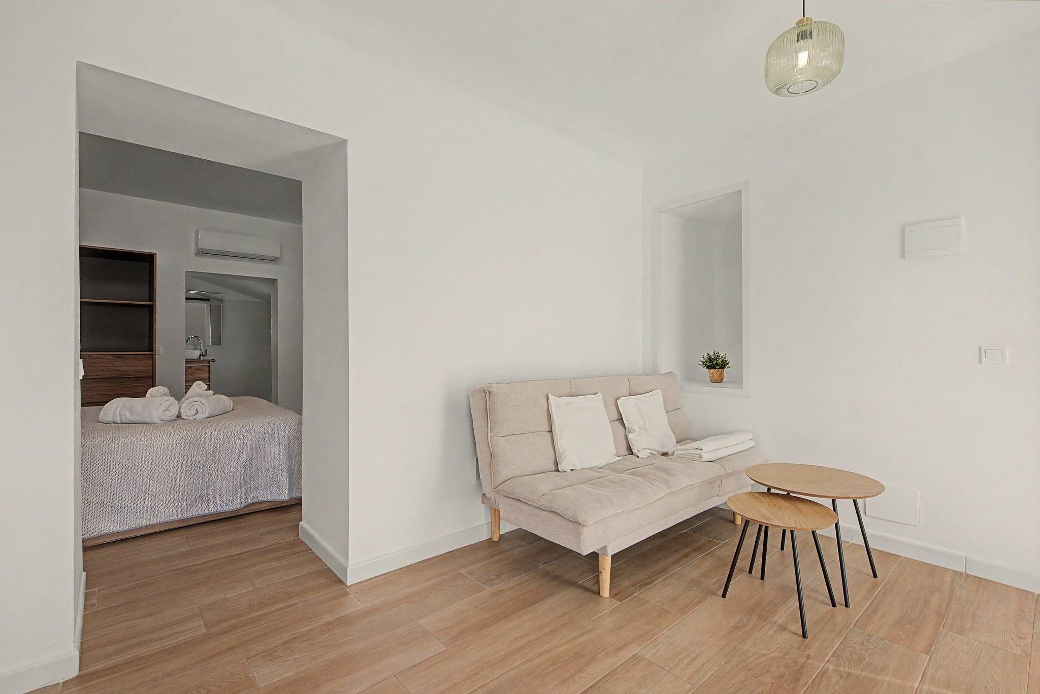 Quarto moderno e minimalista com sofá bege, uma mesinha redonda e um espelho grande.