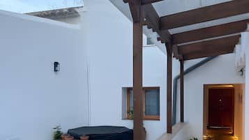 Un patio moderno al aire libre con zona de estar, una pérgola cubierta y suelo de madera que conduce a un pasillo interior.
