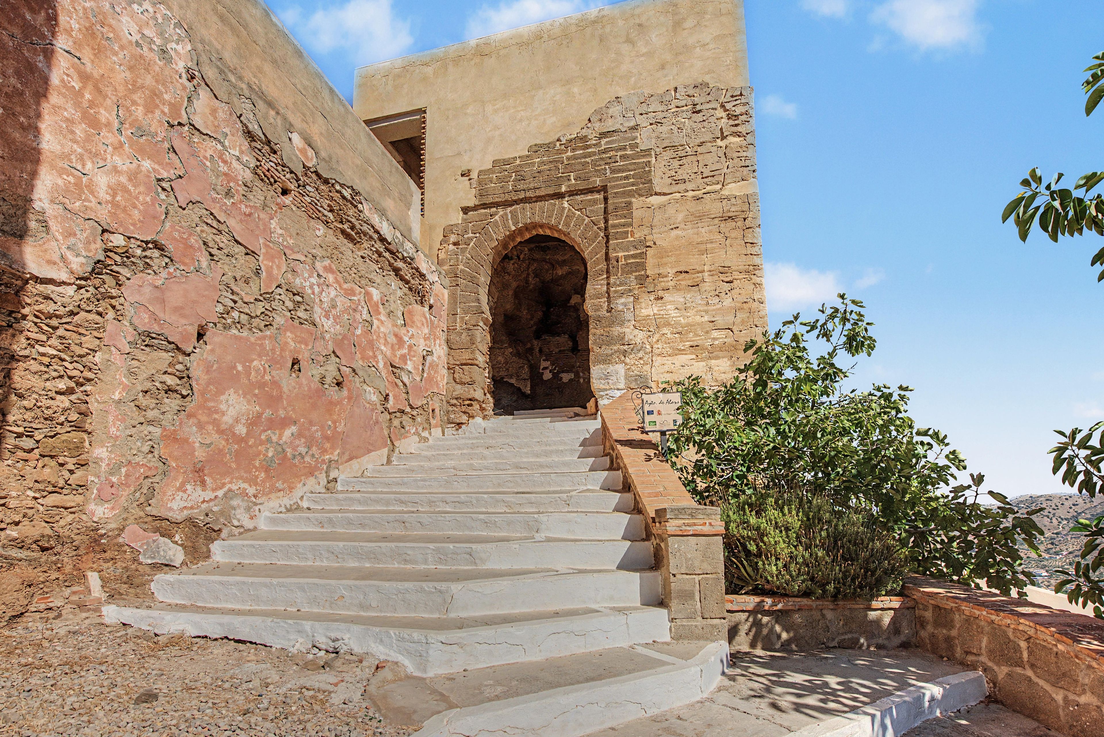Un escalier en pierre menant à une porte en arc de cercle, entouré de murs anciens et surplombant un ciel dégagé.