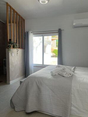 Et soveværelse med en seng, et vindue med gardiner, en plante og en aircondition.