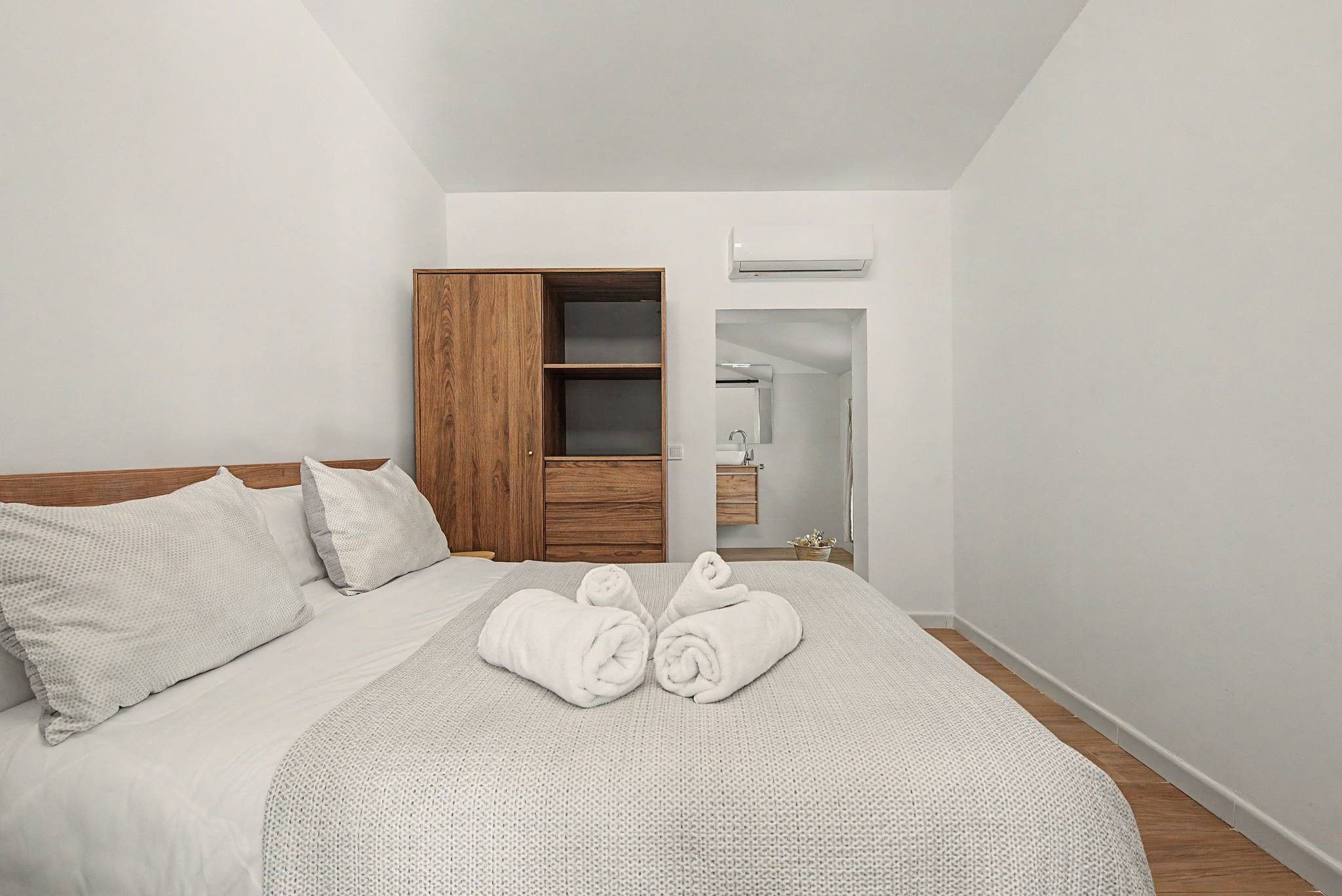 Quarto de hotel com uma cama, um guarda-roupa de madeira, um banheiro com espelho e uma toalha na cama.