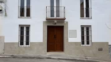 Un edificio de dos pisos con una puerta de madera central, varios ventanales con rejas y un pequeño balcón con barandilla.