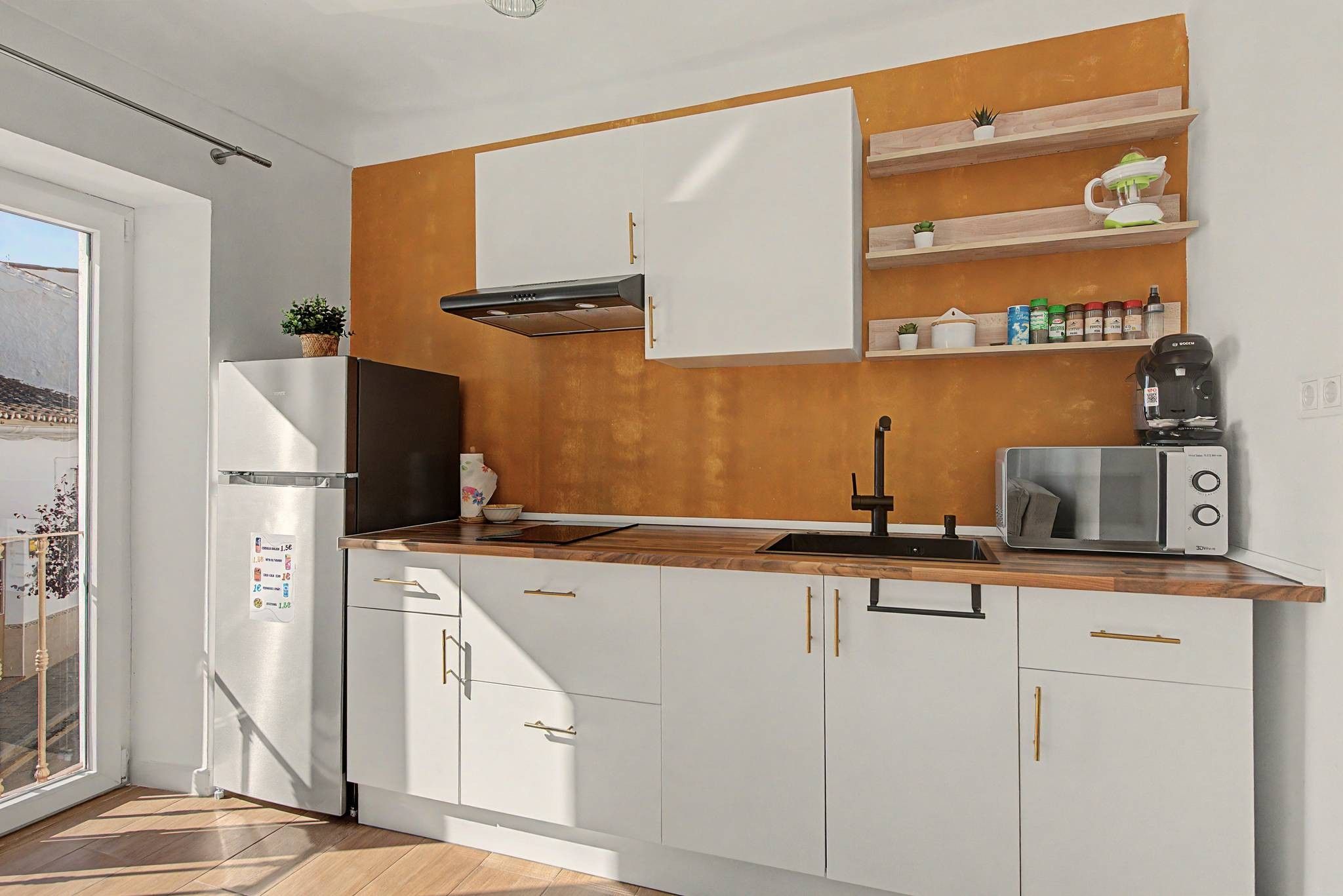 A modern kitchen with white cabinets, a wooden countertop, a built-in stove, and a coffee maker.