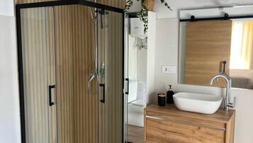 A modern bathroom with a glass-enclosed shower, a wooden vanity with a vessel sink, and a mirror above the sink.