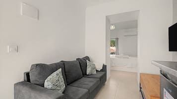 A modern living room with a grey sofa, a flat-screen TV, and a kitchen area with a refrigerator.