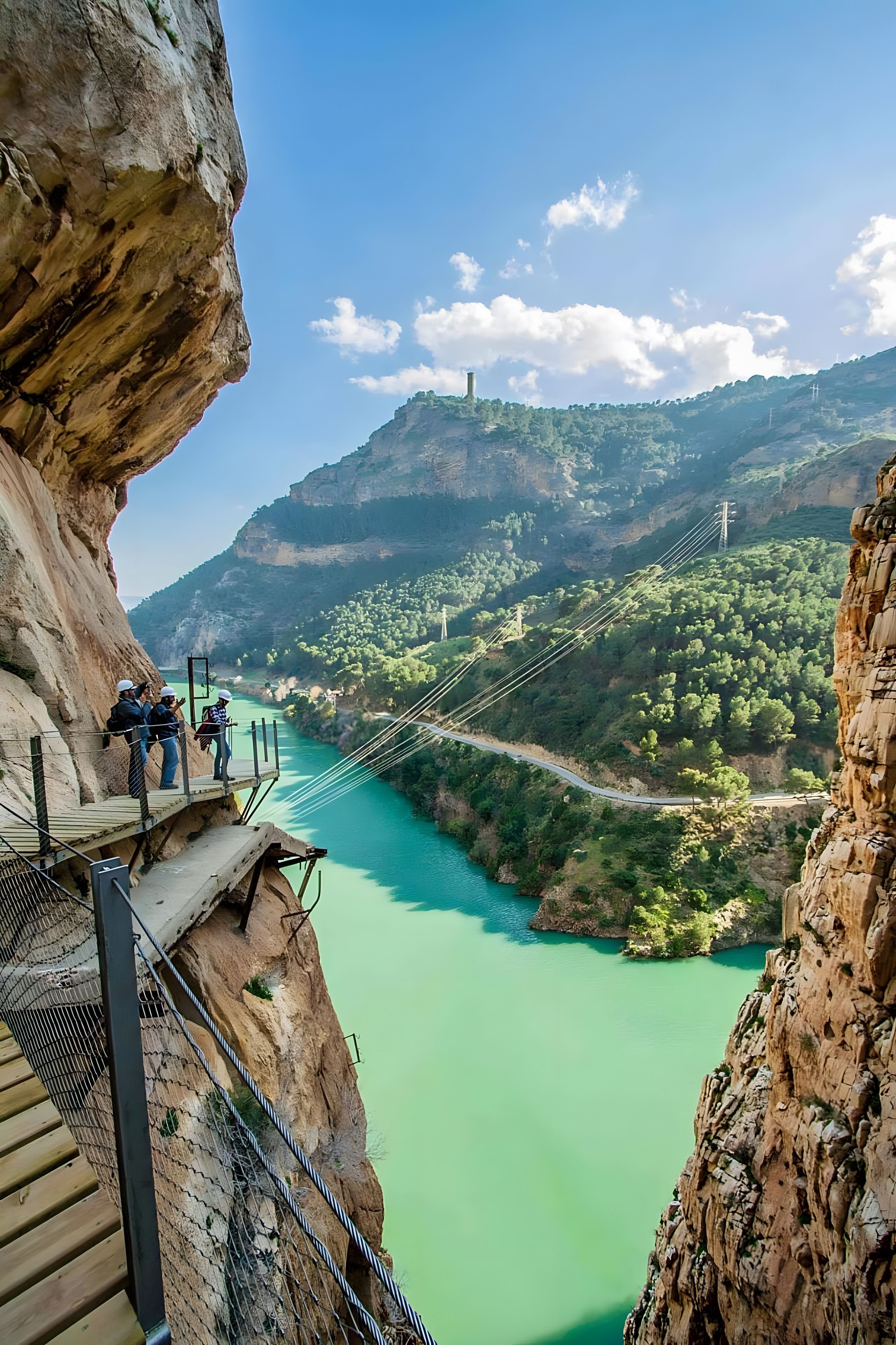 A suspension bridge with a wooden walkway, overlooking a turquoise river and green valley.