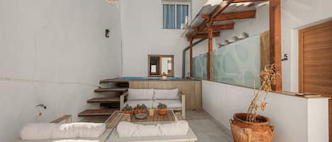 A small outdoor seating area with a wooden table and chairs, a potted plant, and a view of a pool and building in the background.