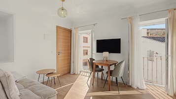 Una sala de estar moderna con un sofá, una mesa de comedor con sillas, un televisor y un balcón con vistas.