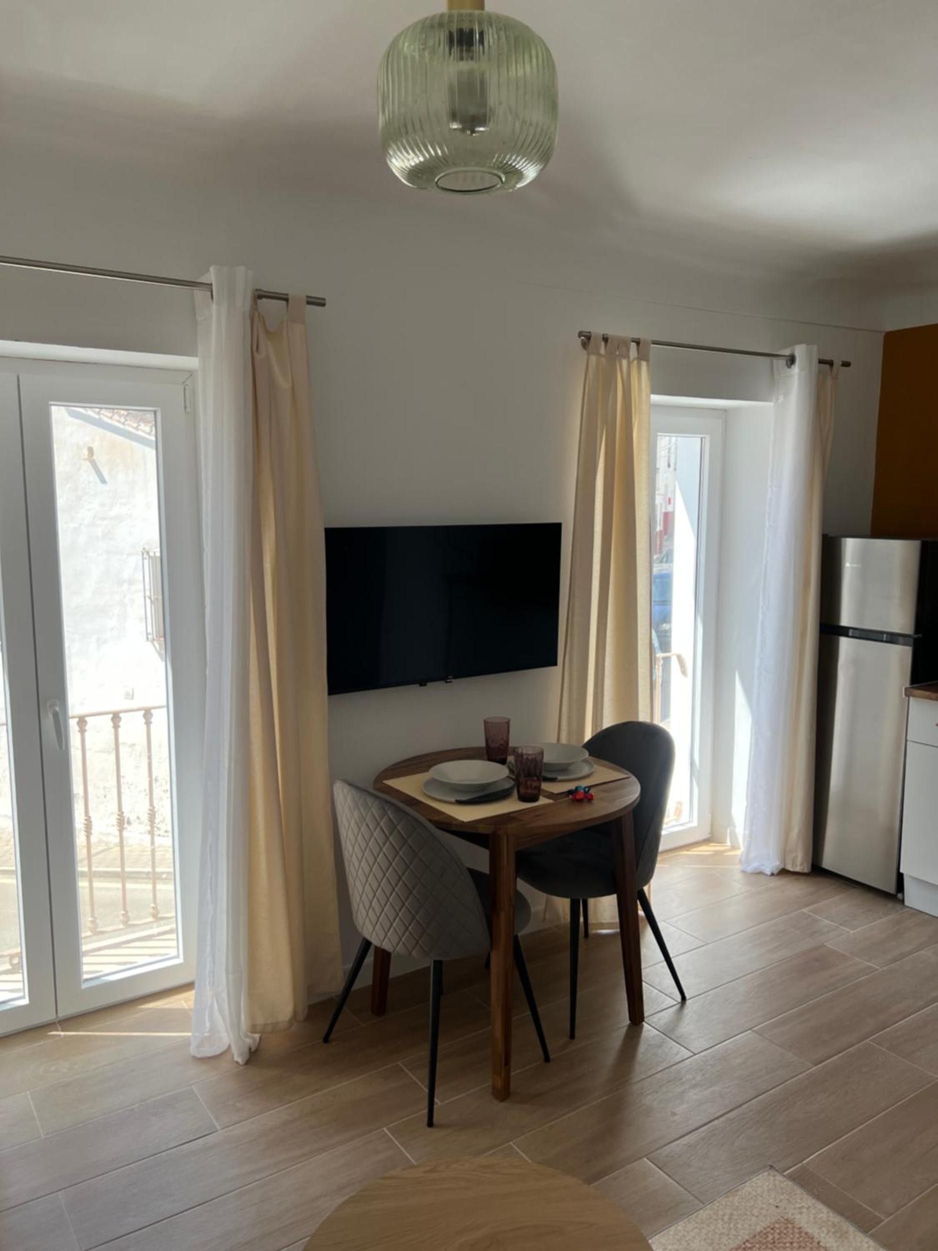Un comedor con una mesa, sillas, un televisor de pantalla plana y una zona de cocina con refrigerador.
