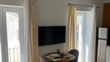 Un comedor con una mesa, sillas, un televisor de pantalla plana y una zona de cocina con refrigerador.