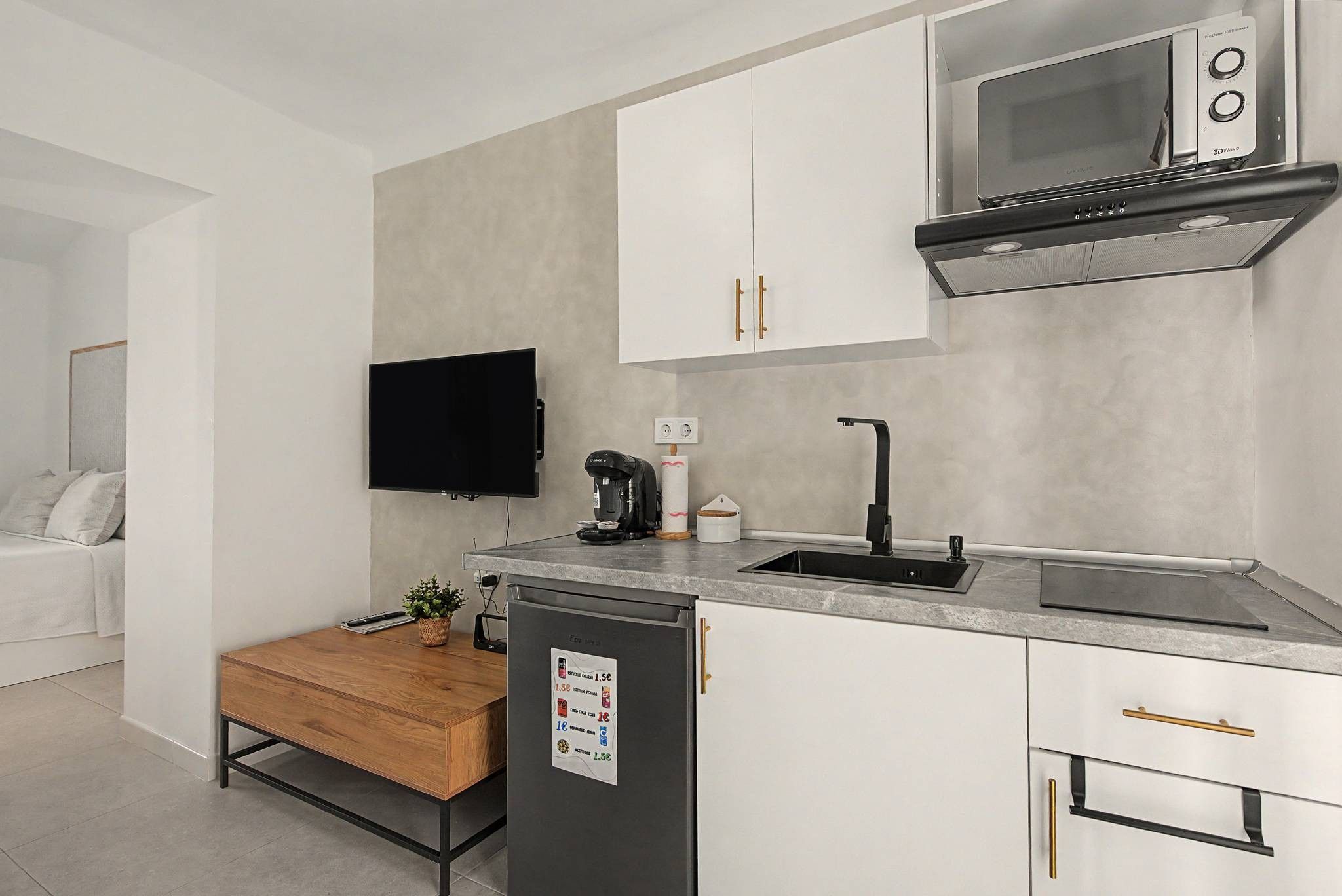 A compact kitchen with a built-in microwave, a coffee machine, and a sink.