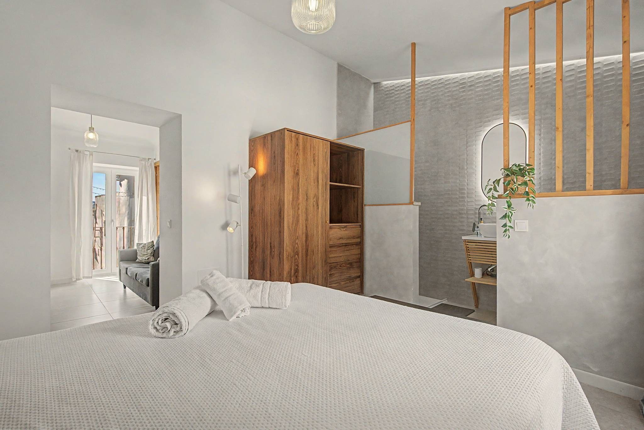 Quarto moderno com cama grande, guarda-roupa de madeira e banheiro com espelho e planta.
