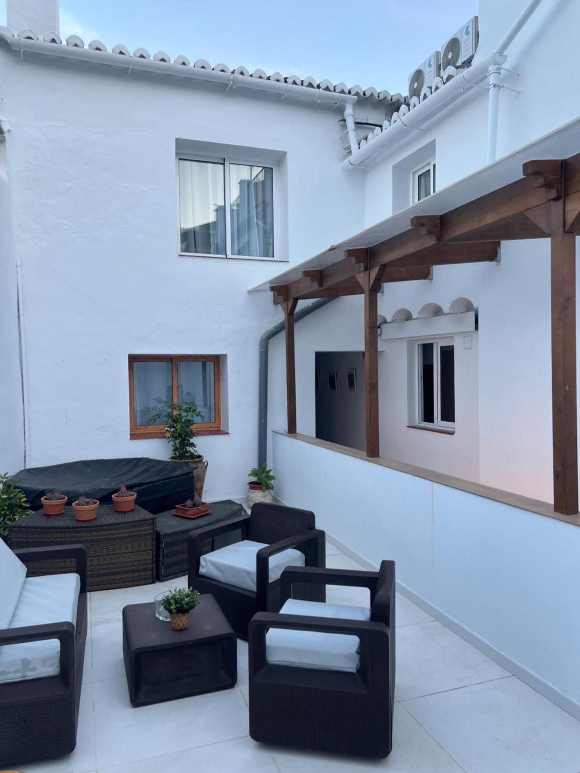 Un espacio patio con mobiliario exterior, plantas en macetas y una estructura pérgola.