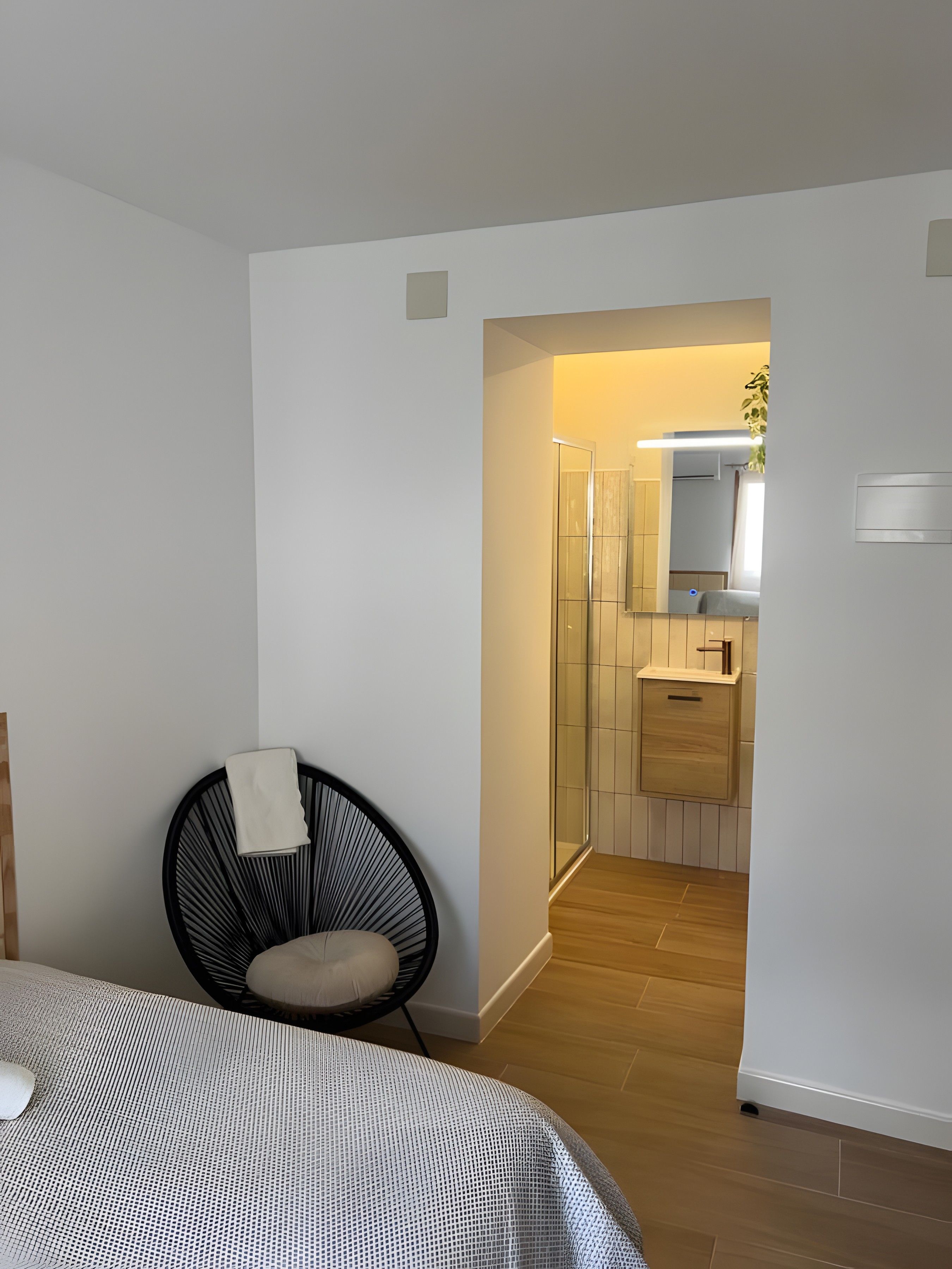 Un dormitorio moderno con cama, una silla y vistas a un baño con ducha y lavamanos.