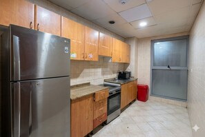 A compact kitchen with wooden cabinets, a stainless steel refrigerator, a microwave, and a stove. - Twin Bed Partition Room Near ICM Metro (Dubai)
