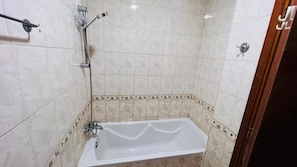 A bathroom with a bathtub, a shower, and a toilet. - Twin Bed Partition Room Near ICM Metro (Dubai)