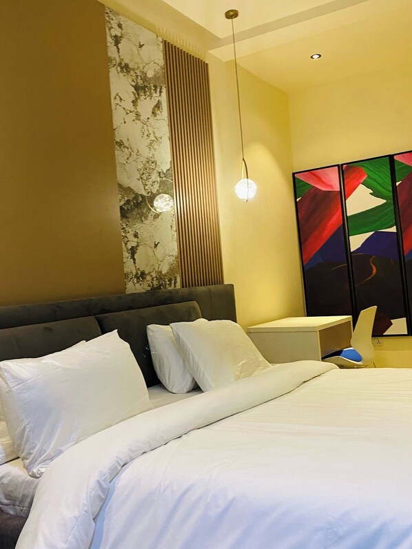 Un dormitorio moderno con una cama grande, cabecera, mesita de noche y una pared con panel decorativo.