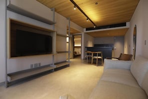 Un salon moderne avec un téléviseur à écran plat fixé au mur, un canapé et un coin repas avec des chaises.
