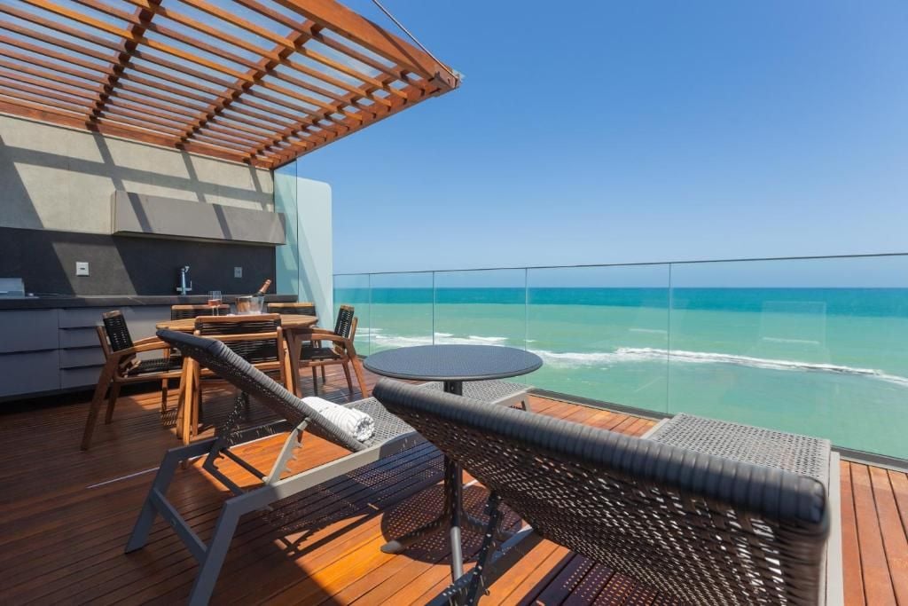 Una terraza con una mesa redonda y sillas, con vista a un mar azul y despejado.