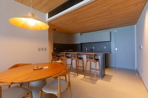 Une cuisine moderne avec un plafond en bois, un coin repas avec une table ronde et des chaises, et un îlot de cuisine avec des tabourets de bar.