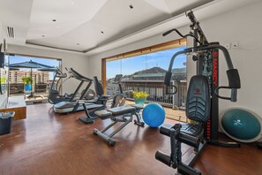 Een sportschool in huis met trainingsapparatuur, uitzicht op gebouwen en een balkon met een plant in een pot.