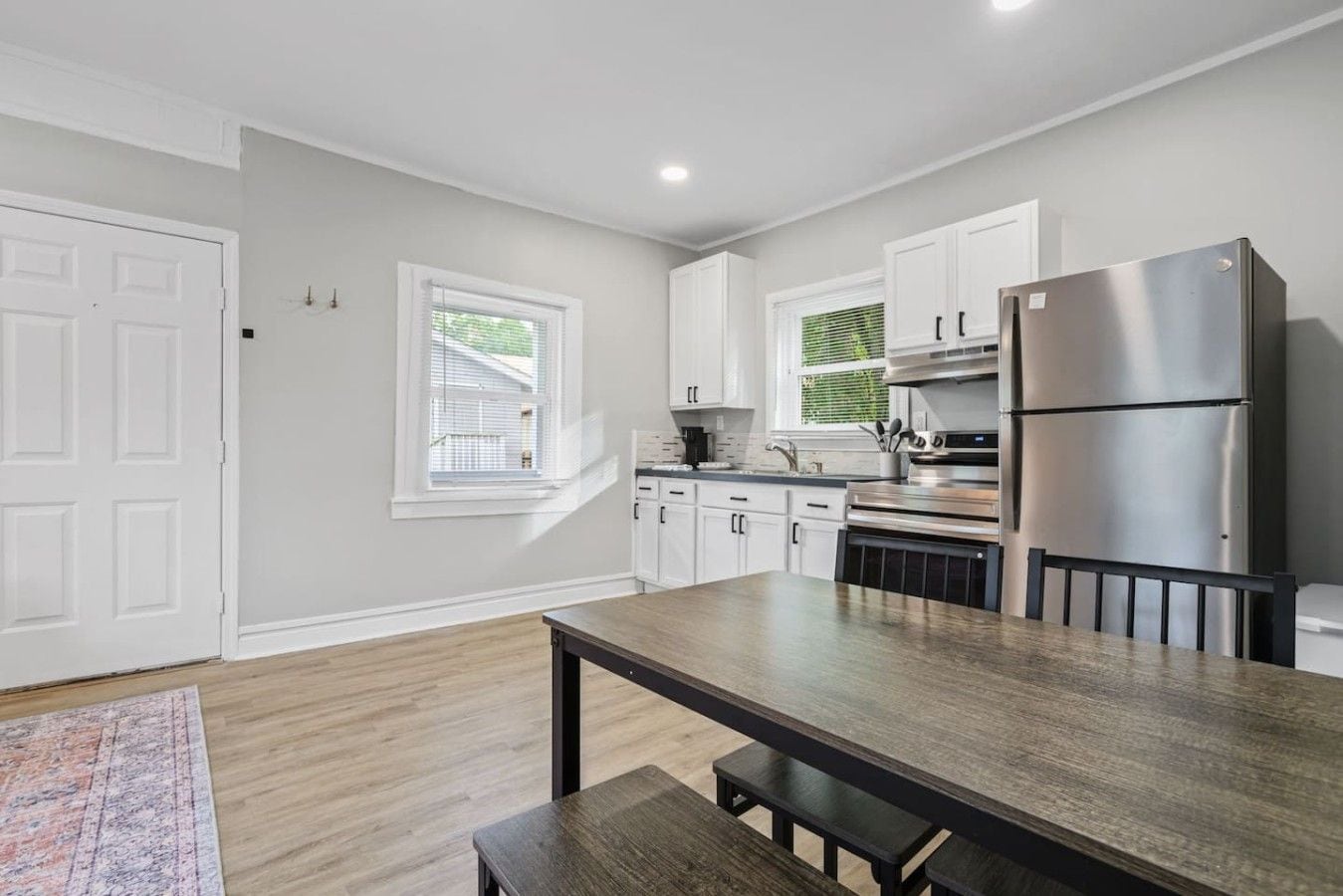 A modern kitchen with white cabinets, a stainless steel refrigerator, and a wooden dining table.