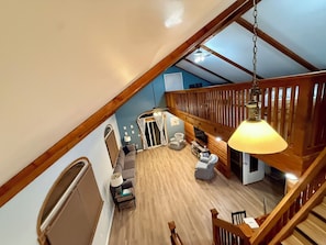 Ein geräumiger Loft mit hoher Decke, Holzbalken, einer Treppe, einer Sitzecke mit Sofa und Sesseln sowie einem Esstisch.